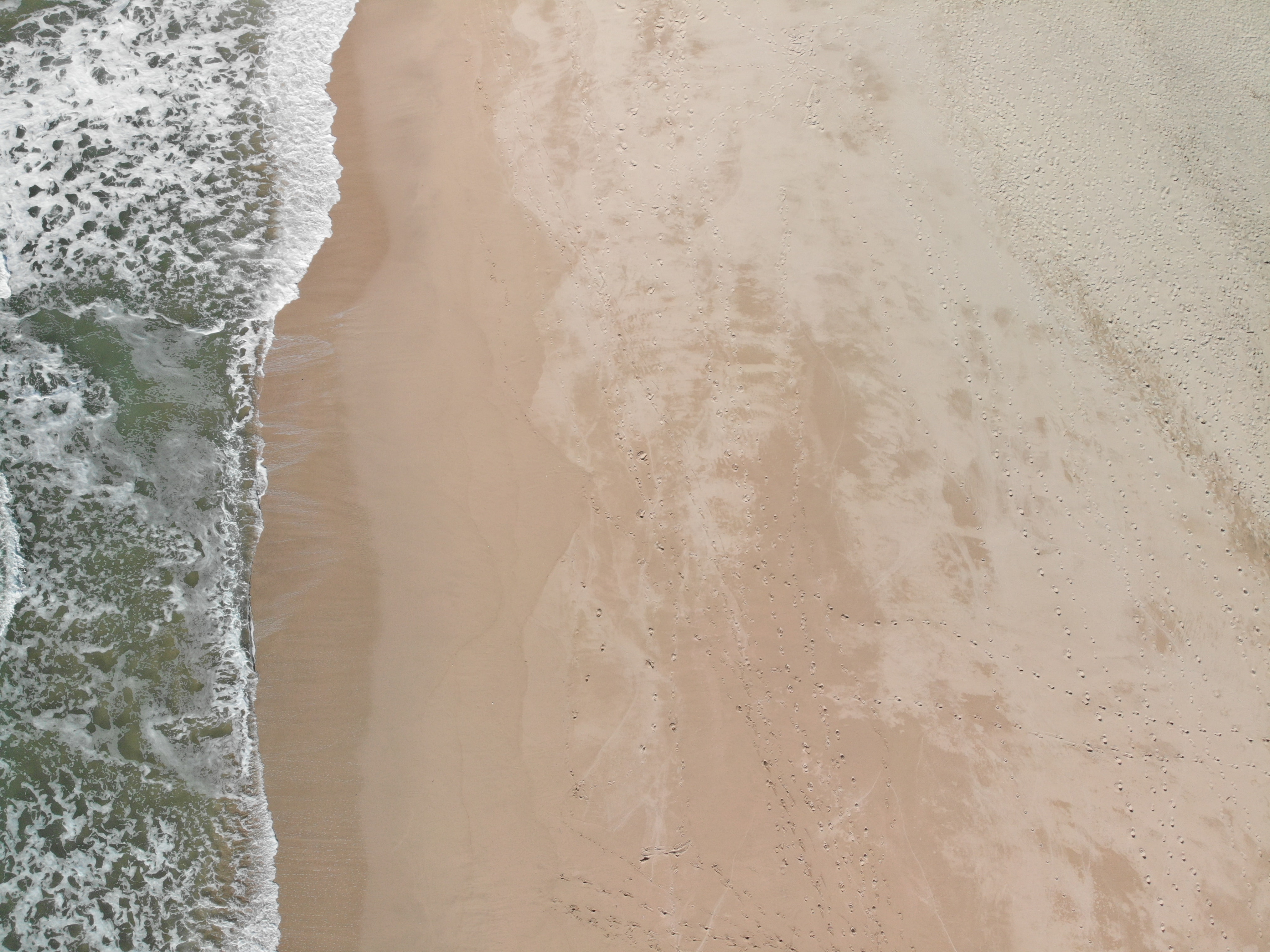 Ocean water meeting a sandy shoreline from above